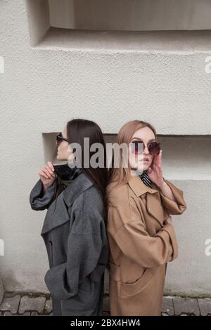 vue latérale de deux modèles portant des manteaux de laine chauds posé sur un fond de mur. vue en grand angle. image de mode de style de rue pour le magazine Banque D'Images