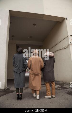 Vue arrière de trois modèles portant des manteaux de laine chauds posant dans le fond de la ville, non reconnaissable. Vue en angle bas. Image de mode de style de rue Banque D'Images