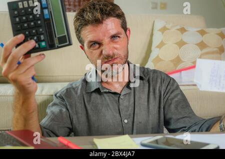 jeune homme stressé et inquiet à la maison salon utilisant la calculatrice et ordinateur portable faire des documents comptables domestiques se sentant submergé sur l'argent impôt ex Banque D'Images