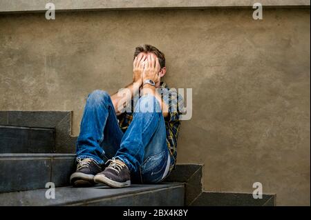 jeune homme triste et désespéré assis à l'extérieur dans les escaliers de rue souffrant d'anxiété et de dépression se sentant misérable pleurer abandonné dans le chômage et Banque D'Images