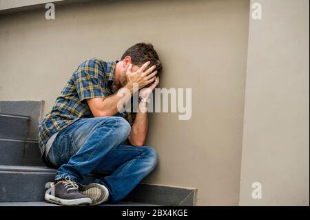 jeune homme triste et désespéré assis à l'extérieur dans les escaliers de rue souffrant d'anxiété et de dépression se sentant misérable pleurer abandonné dans le chômage et Banque D'Images