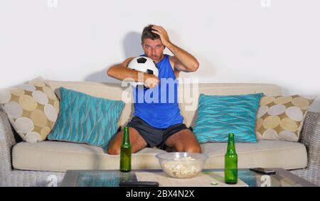 Jeune fan de football et supporter à la maison canapé canapé canapé regardant le match de football à la télévision abattu et triste après la défaite de l'équipe perte et défaite boisson Banque D'Images