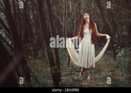 Belle femme de cheveux rouges dansant dans la forêt secrète. Surréaliste et fantaisie Banque D'Images