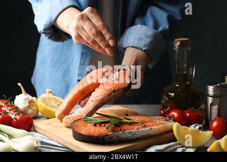 Une femme saupoudrer de sel sur la viande de saumon. Cuisson du saumon sur table grise Banque D'Images