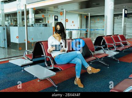Femme lisant son comprimé dans un aéroport avec masque facial protecteur pendant le coronavirus COVID-19 Banque D'Images