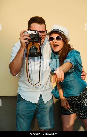 Portrait d'un beau couple de taille basse. Un gars positif dans une chemise et un Jean. Fille en chapeau et lunettes de soleil souriant sur fond jaune Banque D'Images