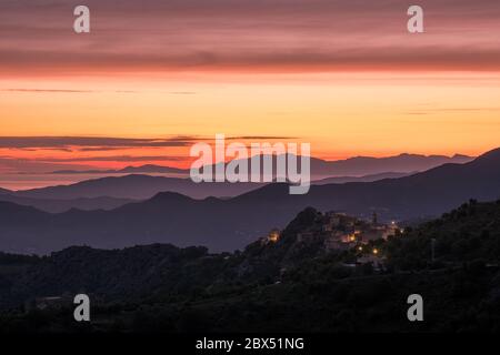 Aube se brisant sur la côte silhouetée du Cap Corse et l'ancien village de montagne de Speloncato en Corse Banque D'Images