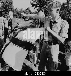 Berlin-Spandau / Nazis / groupes de droite 20.8.1987 devant la prison des criminels de guerre de Spandau, Rudolf Hess vient de mourir. Les groupes de droite se rassemblent en deuil. Le jeune radical de droite Michael Wendt (à droite) avec le drapeau de guerre de Reich et le salut de Kuehnen, une variante du salut d'Hitler, qui a été interdit. Un policier demande ce que c'est. Fleurs devant pour Hess. // nazi / fascisme / *** Légende locale *** la prison pour les criminels de guerre à Berlin-Spandau. Le dernier prisonnier, Rudolf Hess, est mort juste après 46 ans dans la prison montrée en arrière-plan. Aile droite Banque D'Images