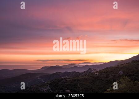 Aube se brisant sur la côte silhouetée du Cap Corse et l'ancien village de montagne de Speloncato en Corse Banque D'Images