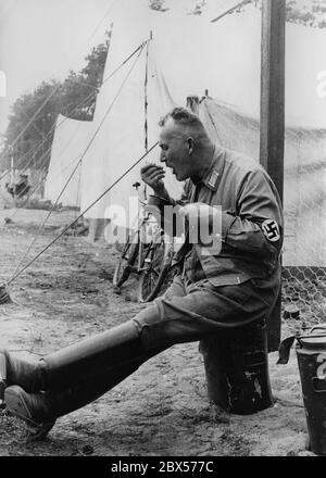 Le Gau Saxe des dirigeants politiques du NSDAP ont installé leurs tentes dans le camp de Langwasser pendant le Congrès du Parti Reich. Un fonctionnaire du parti est assis sur un récipient thermos et mange avec ses doigts du couvercle d'un récipient. Un vélo est penché contre la tente suivante. Banque D'Images