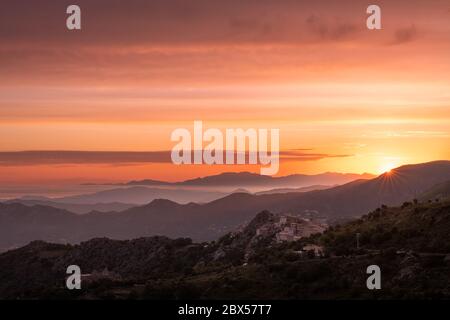 Soleil levant sur la côte silhouetée du Cap Corse et l'ancien village de montagne de Speloncato en Corse Banque D'Images