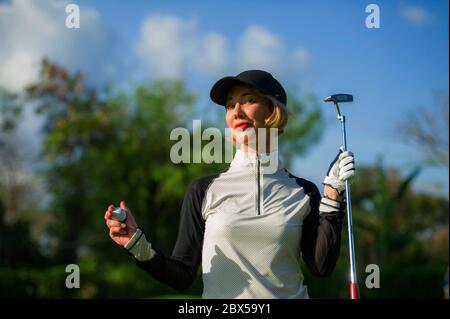 style de vie en plein air portrait de jeune belle et heureuse femme à jouer au golf tenant le ballon et le club de putter souriant gai dans le clothe de golf élégant Banque D'Images