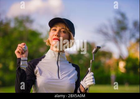 style de vie en plein air portrait de jeune belle et heureuse femme à jouer au golf tenant le ballon et le club de putter souriant gai dans le clothe de golf élégant Banque D'Images