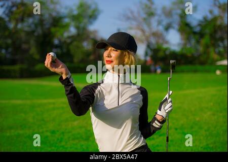 style de vie en plein air portrait de jeune belle et heureuse femme à jouer au golf tenant le ballon et le club de putter souriant gai dans le clothe de golf élégant Banque D'Images