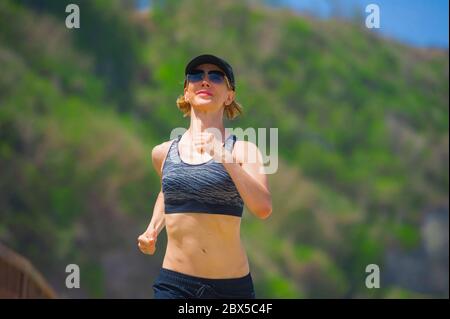 jeune sportive heureuse et attrayante femme faisant courir entraînement en extérieur jogging isolé sur fond de montagne montrant la coupe et le corps athlétique dans Banque D'Images