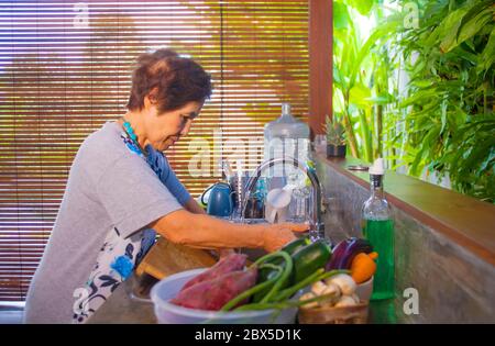 Portrait de style de vie de senior heureux et doux japonais asiatique à la retraite, femme cuisine à la maison seule cuisine propre et propre laver les plats souriant chee Banque D'Images