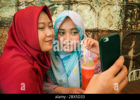 Adolescent musulman étudiant copines selfie. Des filles indonésiennes asiatiques joyeuses et jolies dans un foulard islamique traditionnel hijab tenant le selfie ensemble hav Banque D'Images