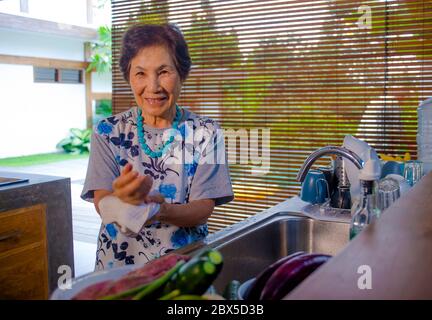 Portrait de style de vie de senior heureux et doux japonais asiatique à la retraite, femme cuisine à la maison seule cuisine propre et propre laver les plats souriant chee Banque D'Images