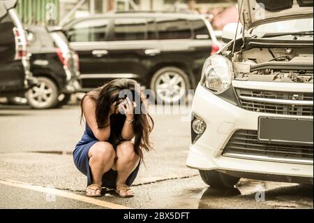 jeune femme désespérée et inquiète en stress, entordue sur le bord de la route avec une panne de moteur de voiture ayant un problème mécanique ayant besoin de réparation et d'assistance Banque D'Images