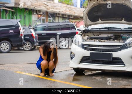 jeune femme désespérée et inquiète en stress, entordue sur le bord de la route avec une panne de moteur de voiture ayant un problème mécanique ayant besoin de réparation et d'assistance Banque D'Images