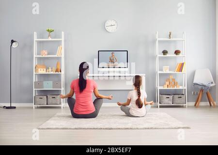 Pratique du yoga en famille. Mère et fille pratique yoga méditation formation en ligne vidéo entraîneur assis sur le sol dans la salle. Banque D'Images