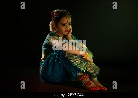 Jeune danseuse de bharatnatyam assise pendant sa représentation devant un fond noir. Banque D'Images