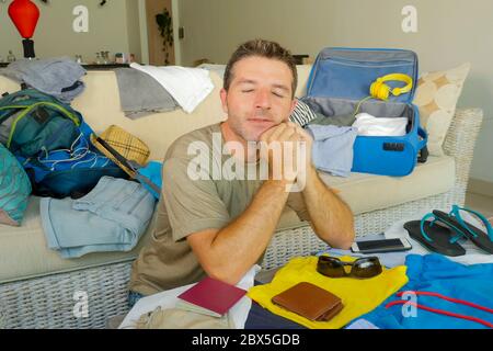 jeune homme attrayant et heureux à la maison canapé préparant le voyage de retour et d'emballage valise pliante vêtements et d'organisation de passeport et des choses excitées bef Banque D'Images
