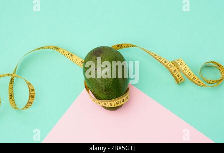 fruit vert avocat et ruban de mesure jaune torsadé sur fond rose vert, concept de régime et de perte de poids, vue du dessus Banque D'Images