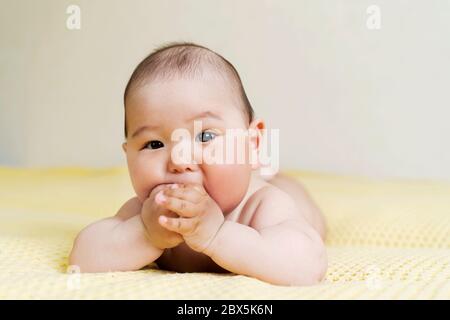 Nouveau-né asiatique mignon garçon tenant les mains dans sa bouche. Dentition. Banque D'Images