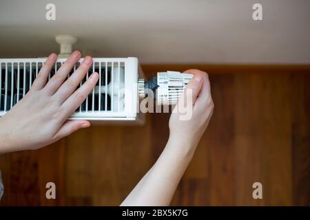 Femme changeant la température sur le radiateur par contrôleur de température, augmenter ou diminuer le prix du chauffage Banque D'Images