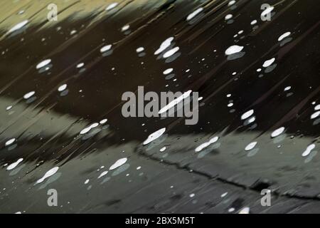 Gros plan de la mousse blanche qui s'abaisse sur la vitre humide de la voiture dans le lave-auto. Verre savonneux du véhicule Banque D'Images
