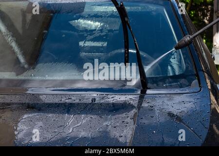 Nettoyage de la voiture avec de l'eau sous haute pression dans la cour arrière. Eau de prière sur la fenêtre avant de la voiture. Banque D'Images