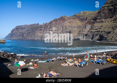 Les gens se baignent au-dessous des falaises de Los Gigantes sur une plage volcanique de sable noir au bord de l'océan Atlantique dans la station balnéaire de Los Gigantes à Tenerife, aux îles Canaries Banque D'Images