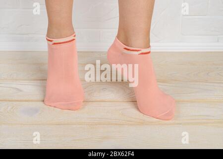 Femme pieds en chaussettes courtes en coton rose debout sur les orteils sur un plancher en bois blanc. Tenez-vous debout sur le pied dans les chaussettes de sport taille basse. Vue avant. Banque D'Images