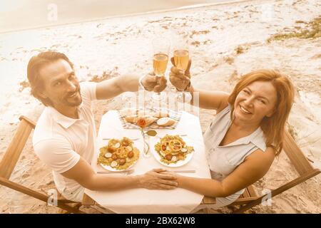 Un couple heureux lève des toasts festifs à l'extérieur. Vue panoramique sur un homme et une femme mûrs souriant qui se trinque avec des verres de vin de cerf-volant tout en étant assis dans un café Banque D'Images