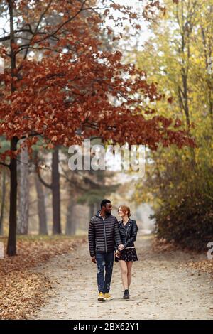 Heureux couple interracial marchant dans le parc d'automne, homme noir et femme rouge blanc Banque D'Images