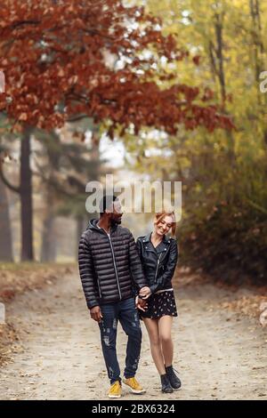 Heureux couple interracial marchant dans le parc d'automne, homme noir et femme rouge blanc Banque D'Images