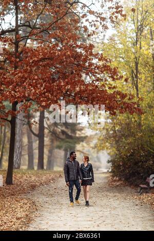 Heureux couple interracial marchant dans le parc d'automne, homme noir et femme rouge blanc Banque D'Images