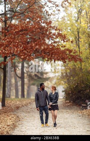 Heureux couple interracial marchant dans le parc d'automne, homme noir et femme rouge blanc Banque D'Images