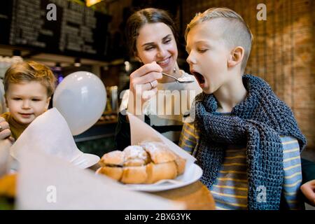 Belle jeune femme avec ses enfants au café, prenant le petit déjeuner avec des croissants frais, des desserts et du café, assis à la table en bois. Heureux Banque D'Images