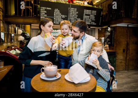 Famille prenant le petit déjeuner au café de la ville avec intérieur flou sur le fond. Les enfants adorables et leurs parents mangeant des croissants frais et savoureux Banque D'Images