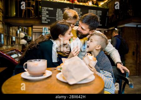 Joyeux famille drôle, père, mère et deux enfants garçons mignons, ayant du fun toégether, tout en s'asseyant dans le café et de prendre leur déjeuner ou petit déjeuner, piquant Banque D'Images