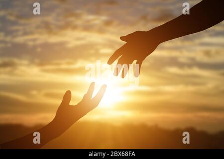 Silhouette de donner une main d'aide, d'espoir et de soutien l'un l'autre sur fond de coucher de soleil. Banque D'Images