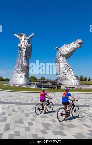 Deux cyclistes qui se trouvent à vélo devant les immenses sculptures de chevaux appelées les Kelpies, près de Falkirk, en Écosse Banque D'Images
