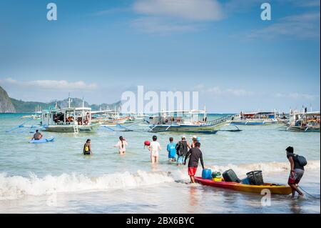 Les touristes et les mains de bateaux philippins locaux se sont emparés ou apportent des fournitures aux nombreux bateaux amarrés dans le surf attendant de visiter les îles et les plages. Banque D'Images