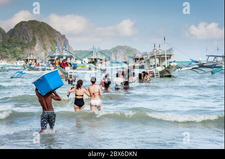 Les touristes et les mains de bateaux philippins locaux se sont emparés ou apportent des fournitures aux nombreux bateaux amarrés dans le surf attendant de visiter les îles et les plages. Banque D'Images