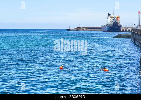 Deux nageurs portant des vêtements visibles dans le port de Douglas à marée haute avec M V Arrow dans backgroundflo Banque D'Images