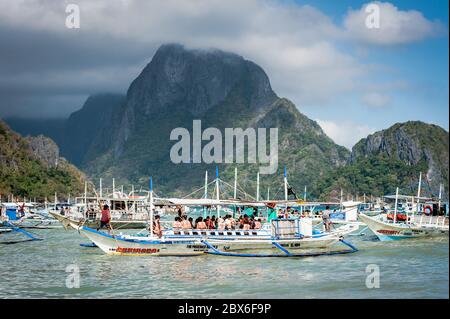 Les touristes et les mains de bateaux philippins locaux se sont emparés ou apportent des fournitures aux nombreux bateaux amarrés dans le surf attendant de visiter les îles et les plages. Banque D'Images