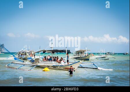 Les touristes et les mains de bateaux philippins locaux se sont emparés ou apportent des fournitures aux nombreux bateaux amarrés dans le surf attendant de visiter les îles et les plages. Banque D'Images