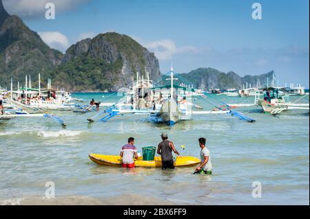 Les touristes et les mains de bateaux philippins locaux se sont emparés ou apportent des fournitures aux nombreux bateaux amarrés dans le surf attendant de visiter les îles et les plages. Banque D'Images